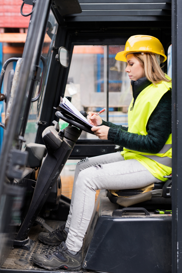 Female forklift truck driver outside a warehouse. A woman sitting in the fork lift making notes.