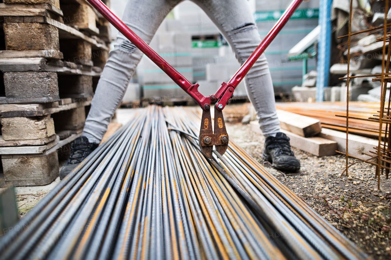 Unrecognizable female worker with bolt cutters in an industrial area.