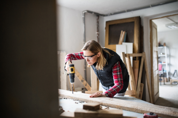 Young woman worker in workroom. Female carpenter using a drill.