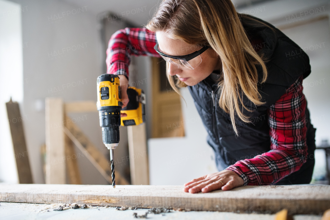 Young woman worker in workroom. Female carpenter using drill.