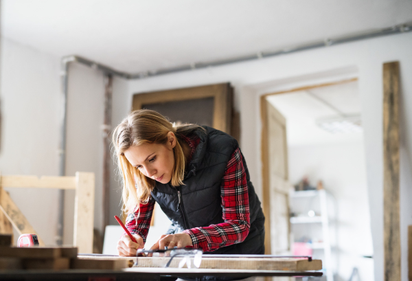 Young woman worker in workroom. Female carpenter measuring wood plank.