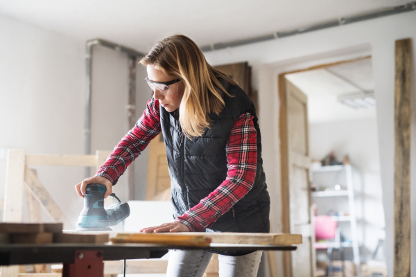 Young woman worker in workroom. Female carpenter using a sander.