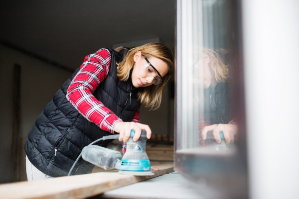 Young woman worker in workroom. Female carpenter using angle grinder.