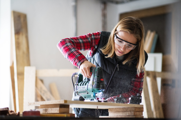 Young woman worker in workroom. Female carpenter using electric saw.