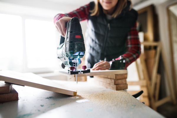 Young woman worker in workroom. Female carpenter using electric saw.