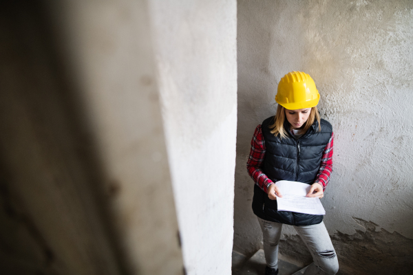 Female worker on the building site. Beautiful young woman holding blueprints. House construction.