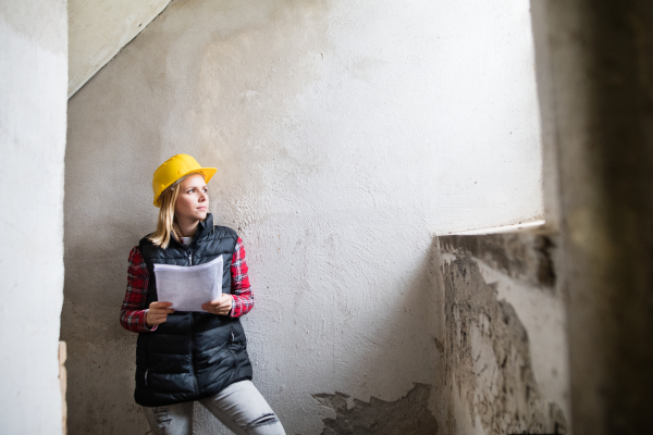 Female worker on the building site. Beautiful young woman holding blueprints. House construction.