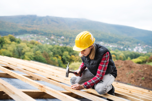 Female worker on the building site. Young woman working as a roofer. House construction.