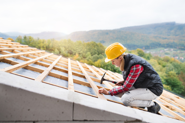 Female worker on the building site. Young woman working as a roofer. House construction.