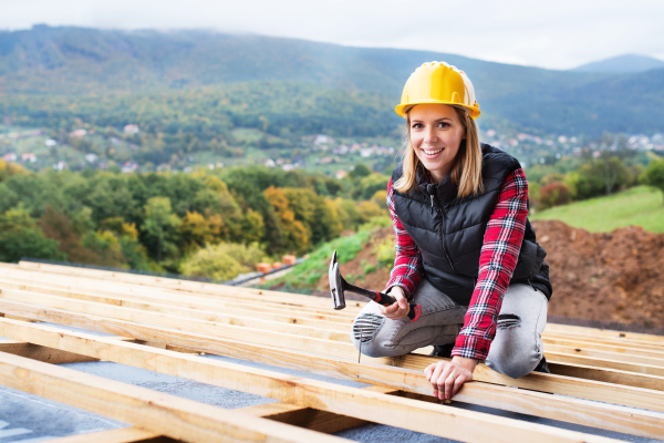 Female worker on the building site. Young woman working as a roofer. House construction.