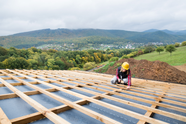 Female worker on the building site. Young woman working as a roofer. House construction.