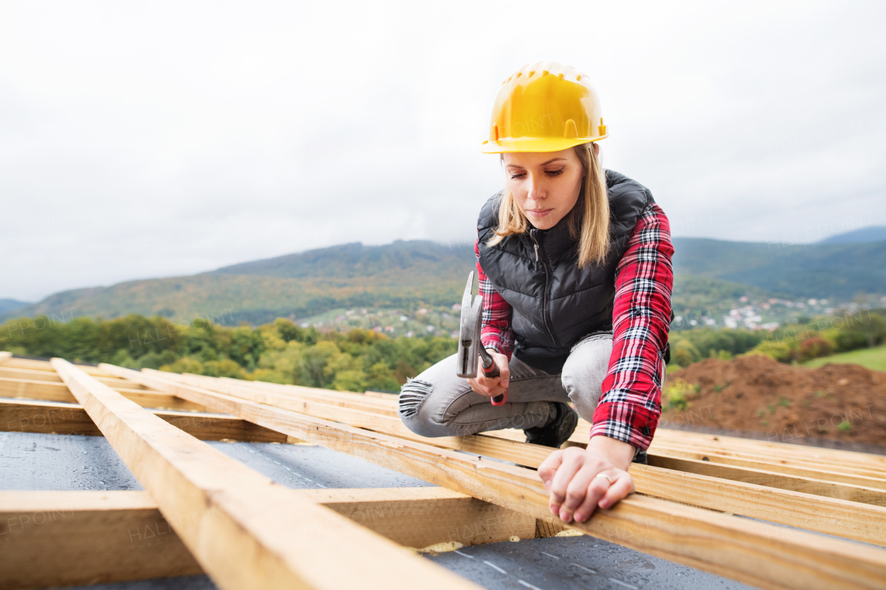 Female worker on the building site. Young woman working as a roofer. House construction.