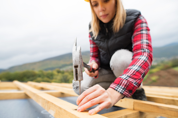 Female worker on the building site. Young woman working as a roofer. House construction.