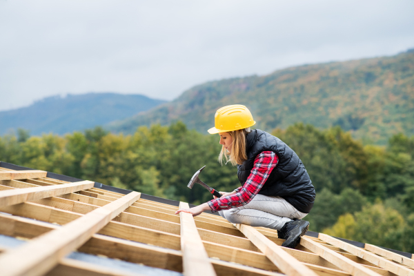 Female worker on the building site. Young woman working as a roofer. House construction.