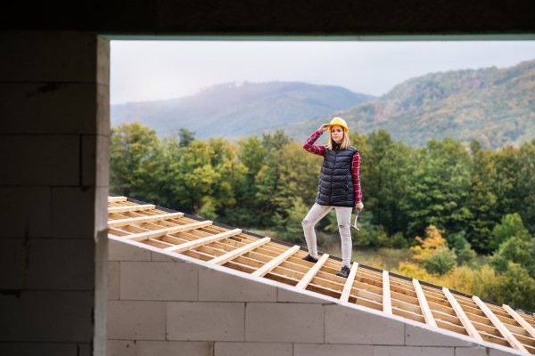 Female worker on the building site. Young woman working as a roofer. House construction.