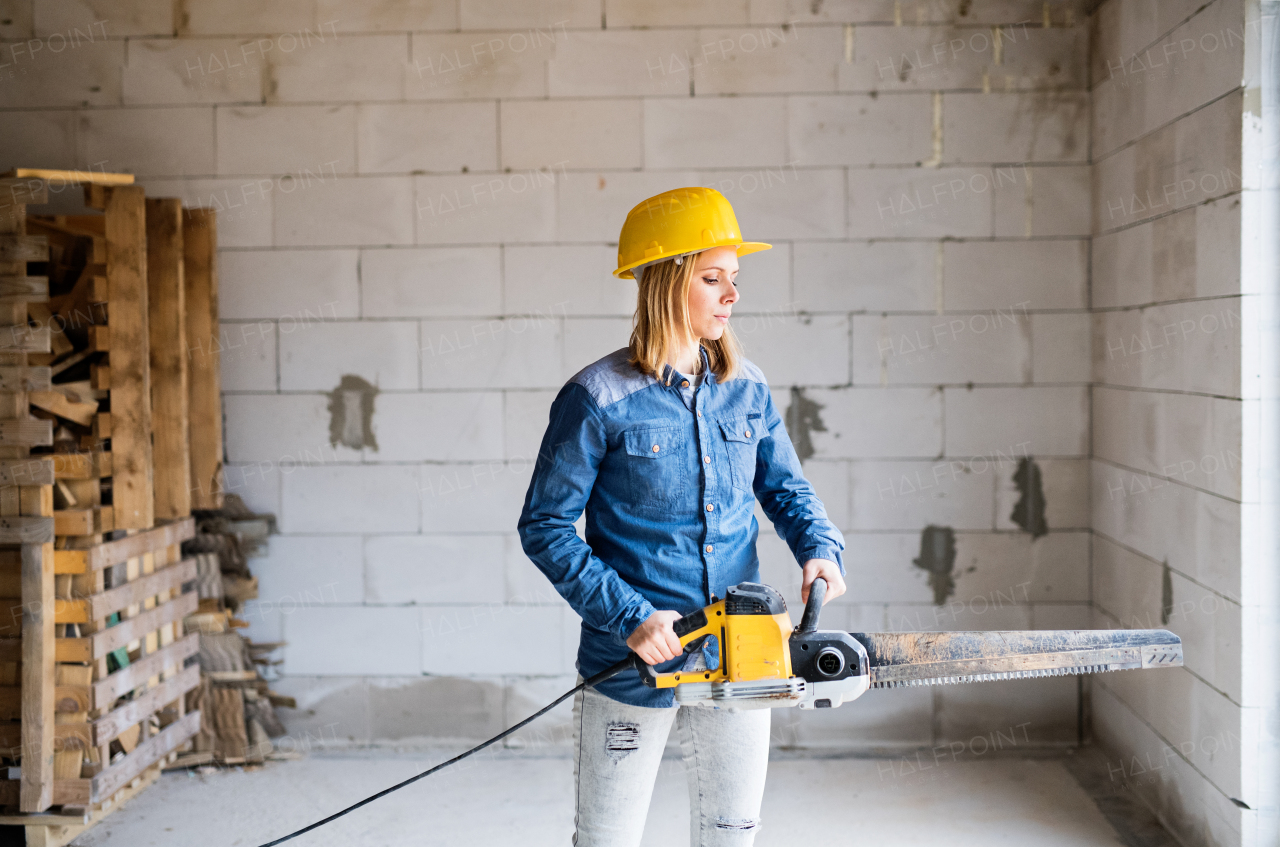 Female worker on the construction site. Beautiful young woman with a saw for cutting blocks.