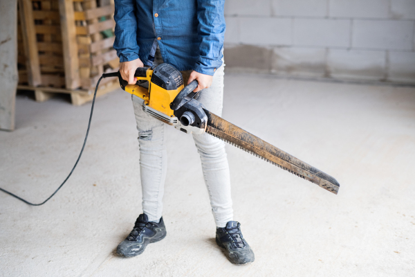 Unrecognizable female worker on the construction site. Young woman with a saw for cutting blocks.