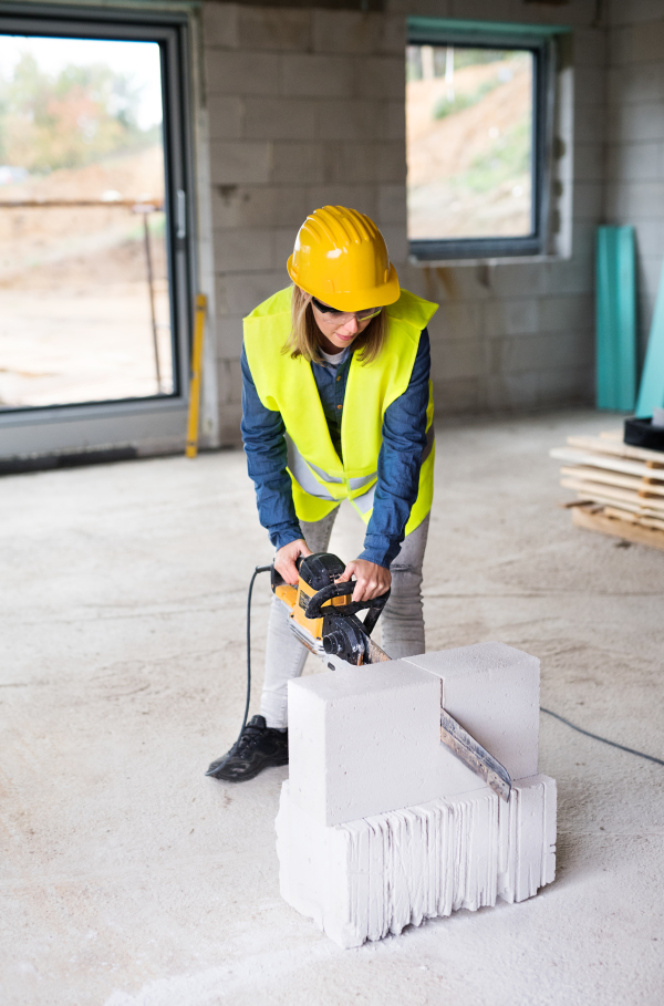 Female worker on the construction site. Beautiful young woman cutting building blocks with a saw.