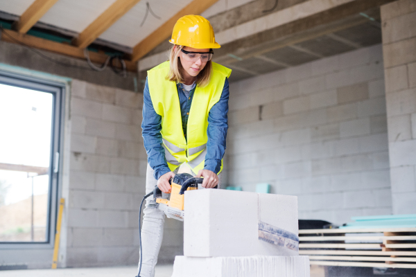 Female worker on the construction site. Beautiful young woman cutting building blocks with a saw.