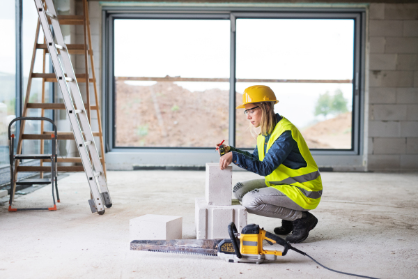 Female worker on the building site. Beautiful young woman measuring the building blocks. House construction.