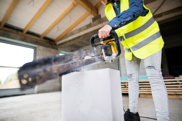 Unrecognizable female worker on the construction site. Beautiful young woman cutting building blocks with a saw.