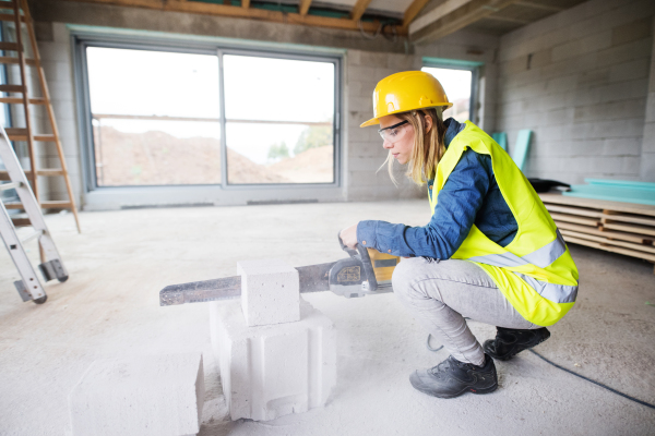 Female worker on the construction site. Beautiful young woman cutting building blocks with a saw.