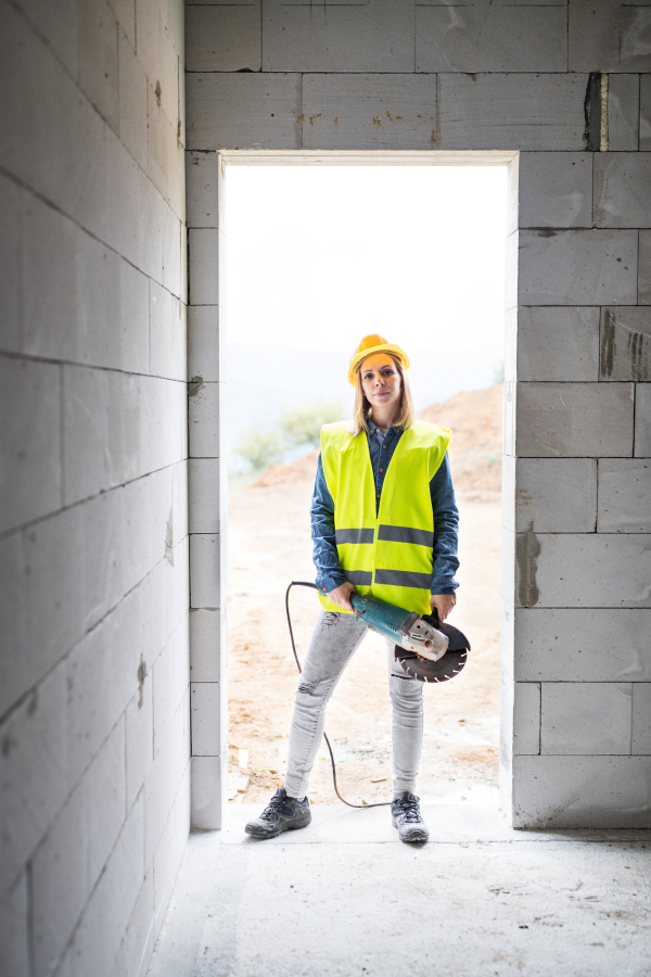 Female worker on the construction site. Beautiful young woman standing with electric tool.