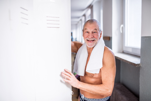 Senior man standing by the lockers in an indoor swimming pool. Active pensioner enjoying sport.