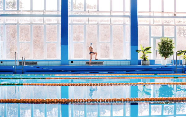 Senior man standing by the indoor swimming pool, stretching. Active pensioner enjoying sport.