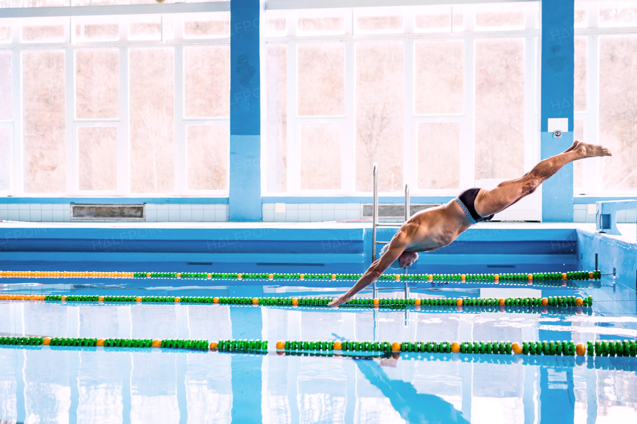 Senior man in an indoor swimming pool. Active pensioner enjoying sport. An old man jumping in the pool.