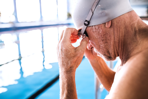 Senior man in an indoor swimming pool. Active pensioner enjoying sport. Close up.