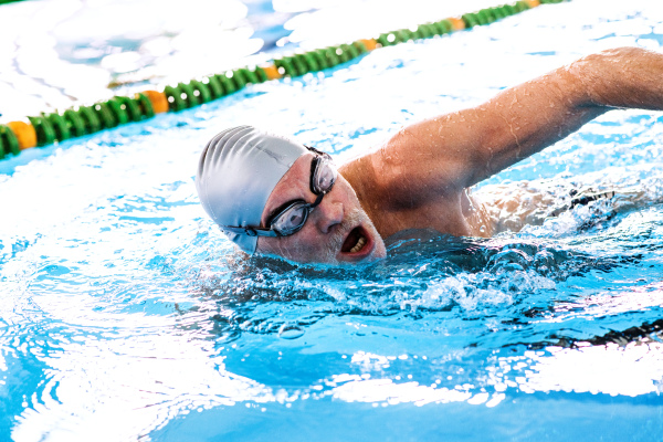 Senior man swimming in an indoor swimming pool. Active pensioner enjoying sport.