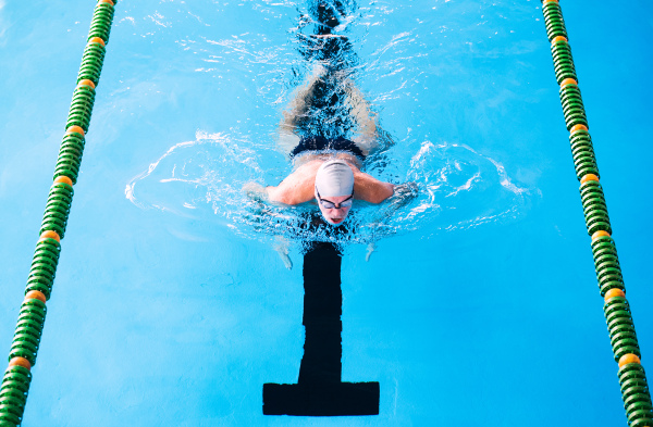 Senior man swimming in an indoor swimming pool. Active pensioner enjoying sport.