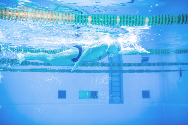 Senior man swimming underwater in an indoor swimming pool. Active pensioner enjoying sport.