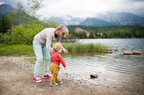 Senior woman with little boy at the lake, summer day. High mountains in the background.