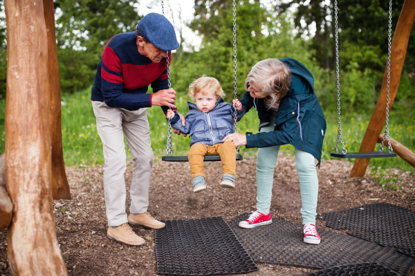 Senior couple with grandson at the playground. Little boy on the swing.