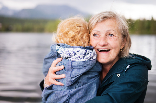 Senior woman with little boy at the lake, hugging. Grandmother with her grandson in the nature.