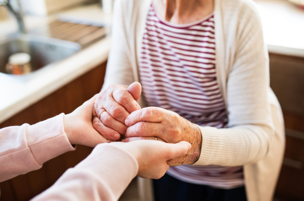 Unrecognizable teenage girl with grandmother at home, holding hands. Family and generations concept. Close up.