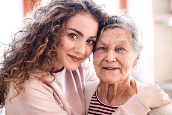 A teenage girl with grandmother at home, hugging. Family and generations concept.