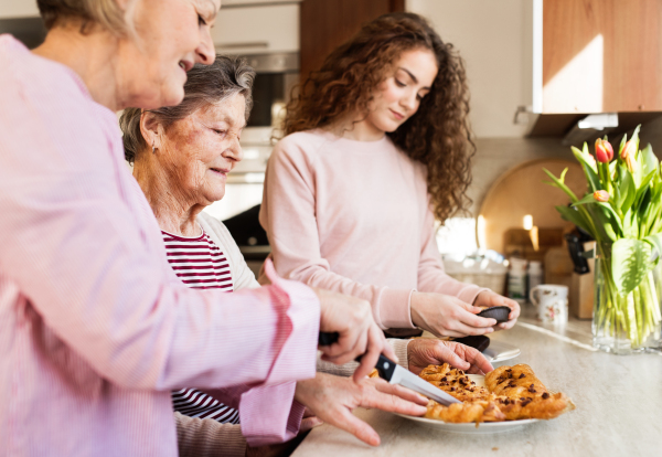 A teenage girl with her mother and grandmother preparing food at home. Family and generations concept.