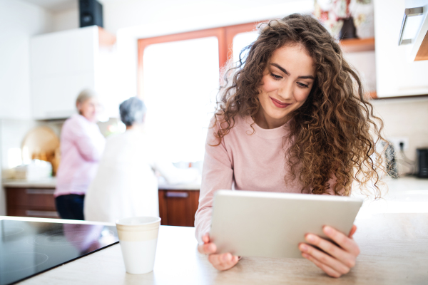 A teenage girl with her mother and grandmother at home, using tablet. Family and generations concept.