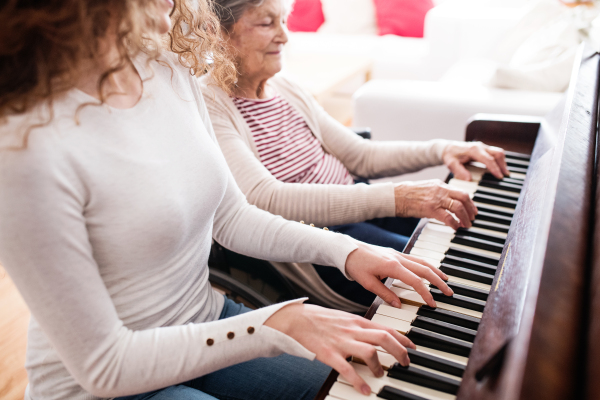 A teenage girl with grandmother in wheelchair playing the piano at home. Family and generations concept.