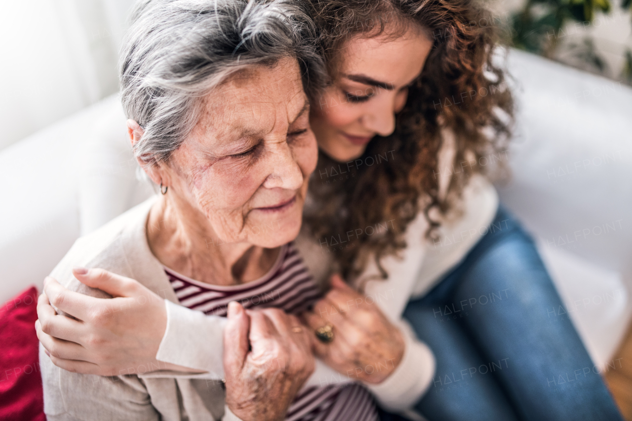 A teenage girl with grandmother at home, hugging. Family and generations concept.