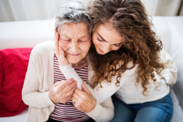 A teenage girl with grandmother at home, hugging. Family and generations concept.