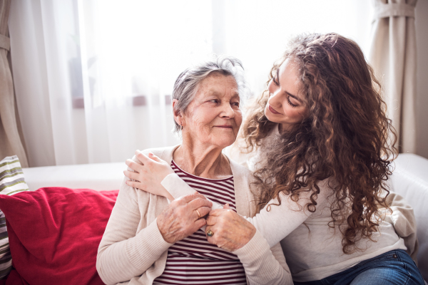 A teenage girl with grandmother at home, hugging. Family and generations concept.