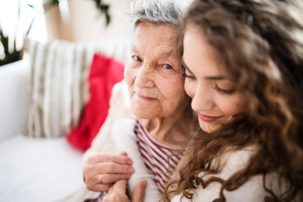 A teenage girl with grandmother at home, hugging. Family and generations concept. Close up.