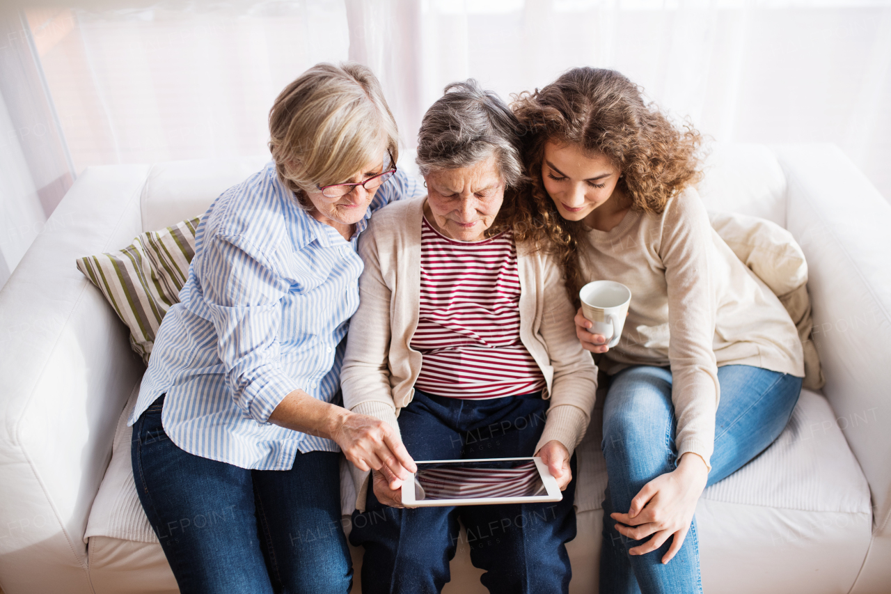 A teenage girl, her mother and grandmother with tablet at home. Family and generations concept.