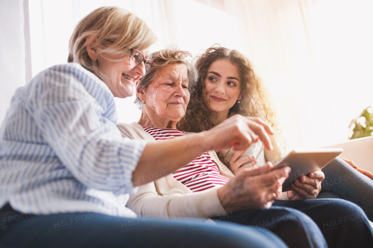 A teenage girl, her mother and grandmother with tablet at home. Family and generations concept.