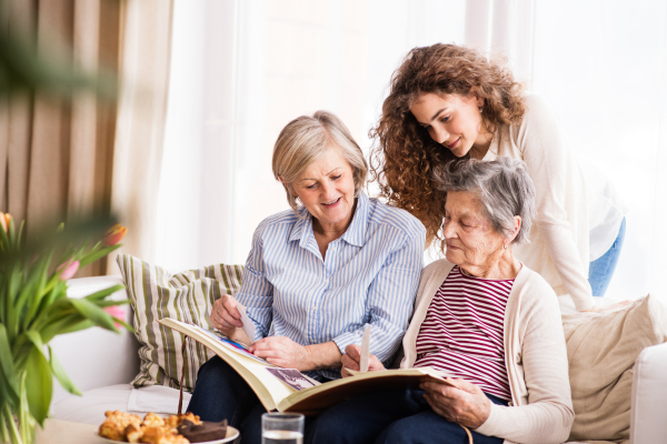 A teenage girl, her mother and grandmother looking at old photographs at home. Family and generations concept.