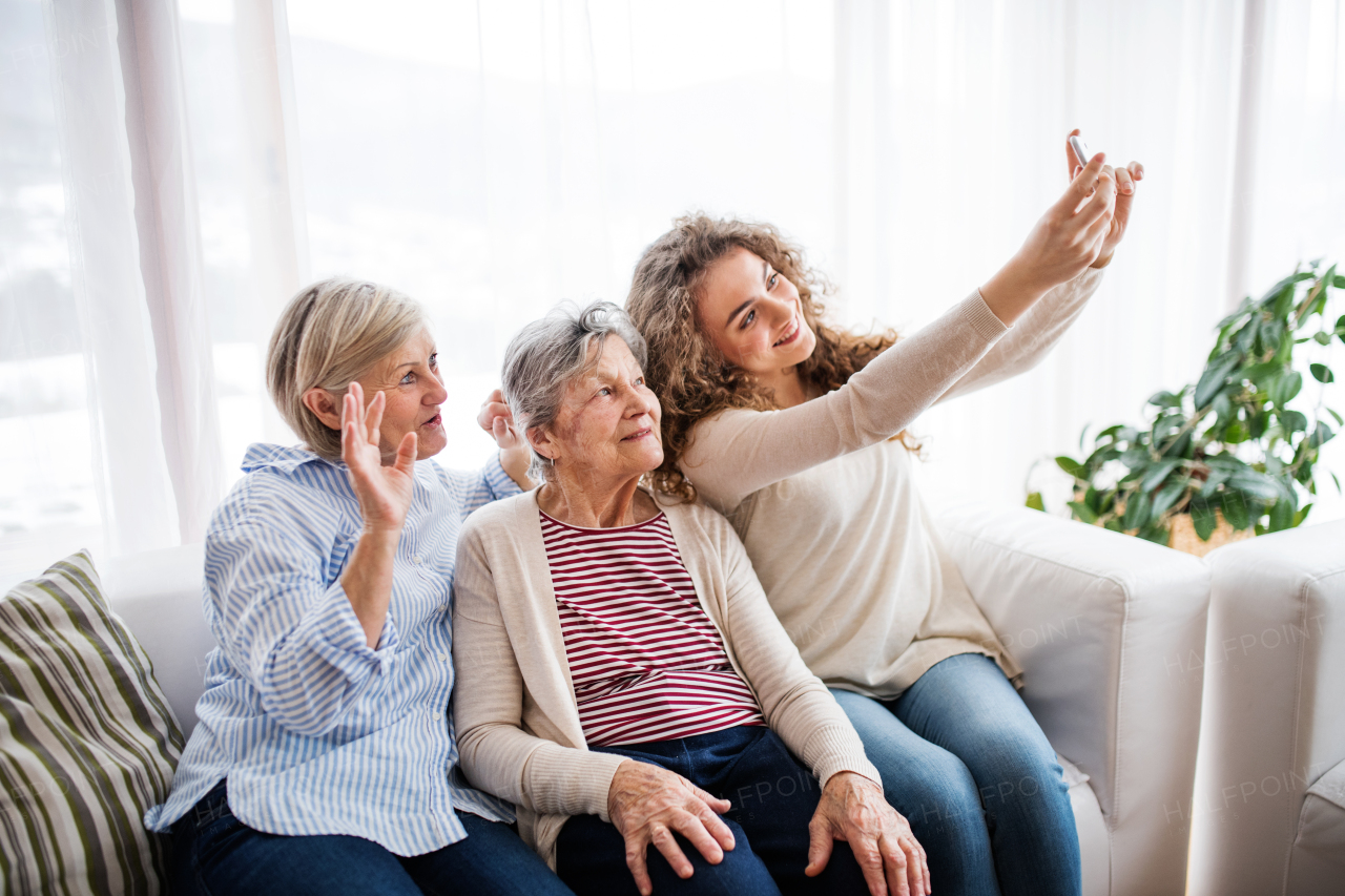 A teenage girl, her mother and grandmother with smartphone at home, taking selfie. Family and generations concept.